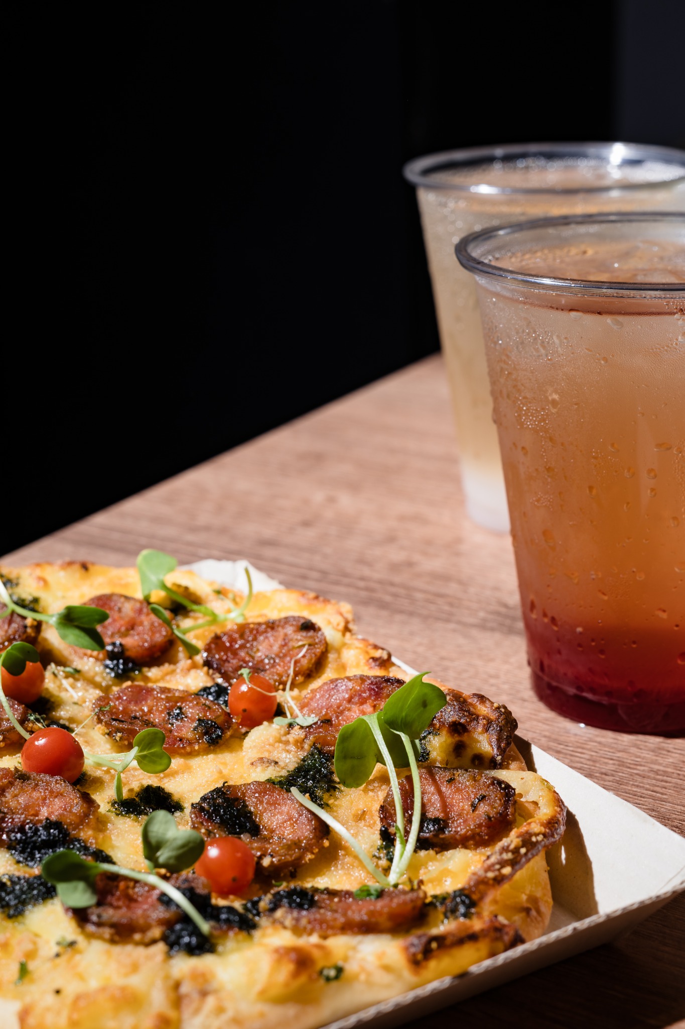 Pizza de La Pate con chorizo, tomates, hojas verdes y bebidas frías
